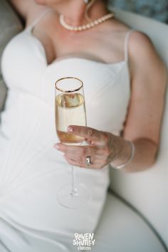 a woman in a white dress holding a wine glass with some liquid on top of it