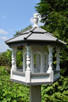 a white and gray gazebo in the middle of some bushes