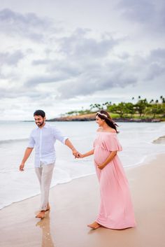 a pregnant couple walking along the beach holding hands