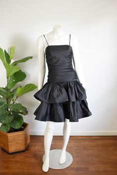 "Description: Black party dress with a drop waist and ruffled skirt. zips up the back and has a large decorative bow. Some tulle under the skirt for fullness.  Bodice has boning up the sides.  Measurements of garment, allow space for fit.  Bust: 32\" has some gathers for cup space. Shown on 36\" and it was way too snug. Waist: 28\" Hips: Open Length: 37\" Skirt length: 15\" I take my measurements flat, and double for circumference.    Tag: No brand, just an ILGWU label.   Fabric: Polyester Condition:  Excellent" Black Party Dress, Under The Skirt, Black Party Dresses, Ruffled Skirt, Black Party, Black Ruffle, Drop Waist, Dresses Xs, Skirt Length