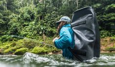 a man standing in the water with a large bag on his back, holding a fishing rod