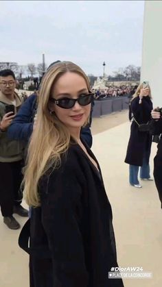 a woman wearing sunglasses standing in front of the washington monument with people taking pictures behind her