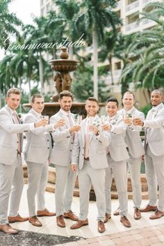 a group of men standing next to each other in front of a fountain holding champagne glasses