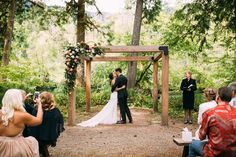 a bride and groom are getting married under an arbor at their wedding in the woods