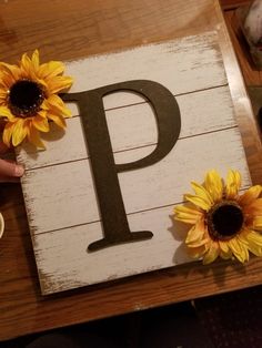 a wooden sign with sunflowers sitting on top of it next to a cup