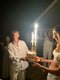 a man and woman holding a cake with sparklers on it in front of other people