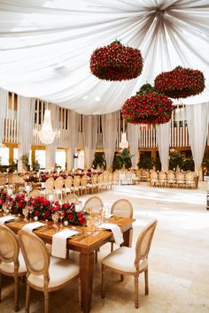 a banquet hall with tables, chairs and chandeliers decorated with red flowers hanging from the ceiling