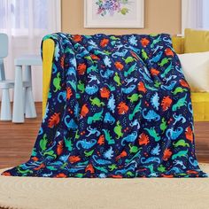 a blue and orange dinosaur print blanket on a rug in front of a yellow chair