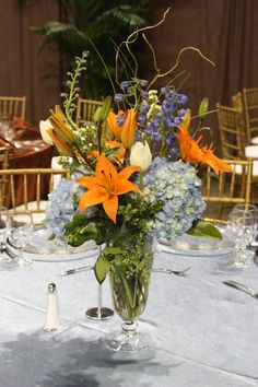 a vase filled with orange and blue flowers on top of a table next to glasses