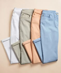 five different colored pants are lined up in a row on a beige background, with one folded and the other unbuttoned