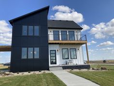 a black house with white windows and balconies on the roof is standing in front of a grassy field