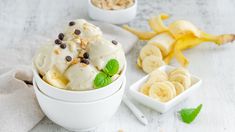 two white bowls filled with ice cream and banana peels next to some sliced bananas