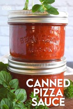 two jars filled with canned pizza sauce sitting on top of a wooden table next to green plants