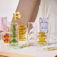 there are many different colored glass vases on the table and one has a flower in it