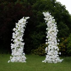 two tall white flowers sitting on top of a lush green field next to bushes and trees