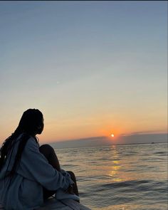 a woman sitting on the edge of a pier watching the sun go down over the ocean