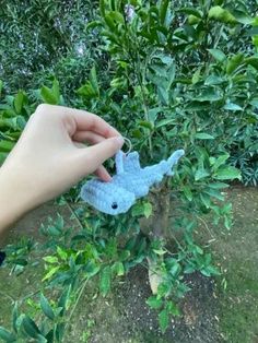 a hand is holding a small blue toy in the grass near some bushes and trees