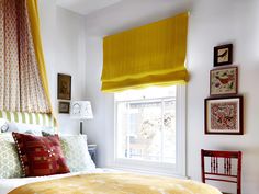 a bedroom with yellow drapes and pictures on the wall above the bed, along with a red chair