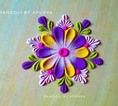 an image of a colorful flower made out of felt on a wooden table with text overlay that reads rangoli by apurva