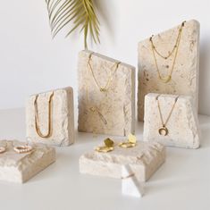 four pieces of jewelry sitting on top of a white table next to a palm tree