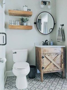 a white toilet sitting next to a wooden cabinet in a bathroom under a round mirror