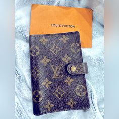 a brown louis vuitton wallet sitting on top of a white blanket next to an orange book