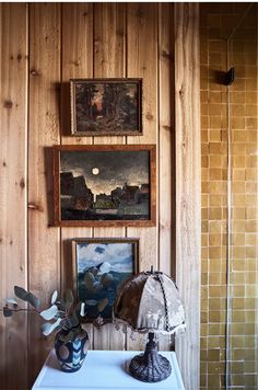 a room with wood paneling and paintings on the wall, including a table lamp