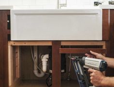 a man is using a drill to fix a sink in a kitchen under the counter