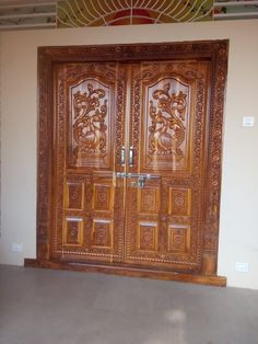 a large wooden door with intricate carvings on the front and side doors, in an empty room