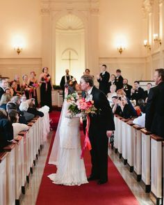 a bride and groom kiss as they walk down the aisle in front of an audience