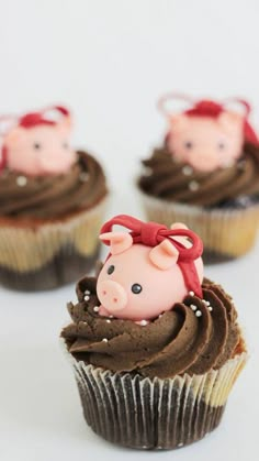 three cupcakes with chocolate frosting and pigs on top, sitting next to each other