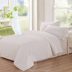 a bed with white sheets and pillows next to a green chair in front of a window