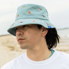 This beautifully embroidered bucket hat details all kinds of beach life found in sand, sea and sky. Can you spot the Piping Plover? You'll also see Horseshoe Crabs, Ruddy Turnstones, Red Knot, Striped Bass and flounder. Playful Bucket Hat For Beach, Playful Bucket Cap For The Beach, Playful Beach Bucket Hat, Summer Beach Bucket Sun Hat, Blue Wide Brim Bucket Hat For Beach, Playful Bucket Hat For Beach Season, Blue Bucket Hat For Outdoor Beach Season, Playful Bucket Sun Hat For Beach Season, Coastal Blue Hat For Vacation