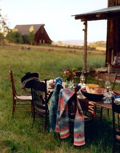 an outdoor table set up for a meal in the middle of a grassy field with a barn in the background