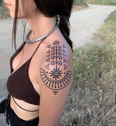 a woman with a black and white tattoo on her shoulder is standing in the grass