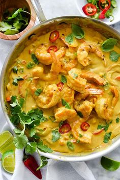 a pan filled with shrimp and yellow sauce on top of a white table next to some vegetables