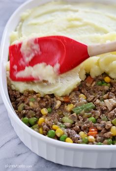 a red spatula scooping mashed potatoes and peas into a casserole dish