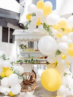 yellow and white balloons are hanging from the side of a table with an old wagon