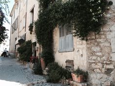 an alley way with potted plants on the side and stone buildings in the background