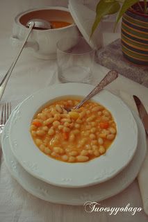 a white plate topped with beans and carrots next to silverware on a table