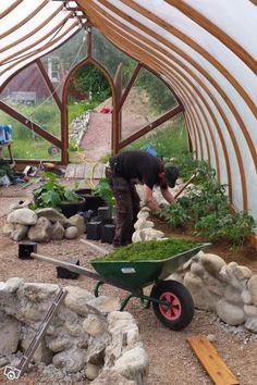 a man is tending to plants in a garden with a wheelbarrow full of dirt