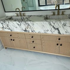 a bathroom vanity with marble top and two sinks in front of a large mirror on the wall