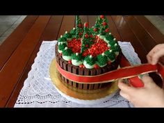 someone is cutting into a christmas cake with red ribbon on the table next to it