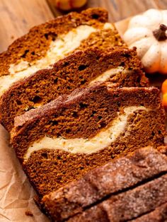 sliced loaf of pumpkin bread with white frosting on top and small pumpkins in the background