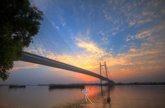 the sun is setting behind a bridge over water