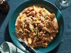 a blue plate topped with pasta and meat next to a glass of wine on top of a table