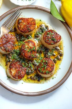 a white plate topped with scallops covered in sauce and garnished with parsley