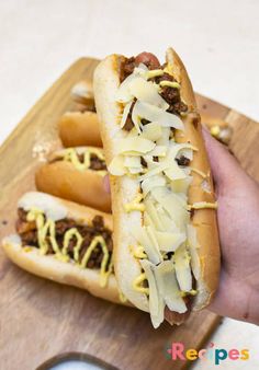 two hot dogs on buns with toppings being held by a person's hand