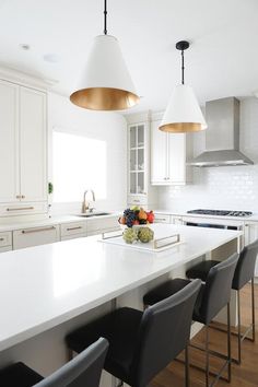 a kitchen with white cabinets and an island in the middle is lit by two pendant lights