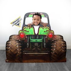 a young boy sitting in the back of a monster truck with his arms out and smiling